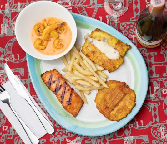 Delicious Colombian seafood platter featuring shrimp, fried plantains, and fish with a creamy sauce.