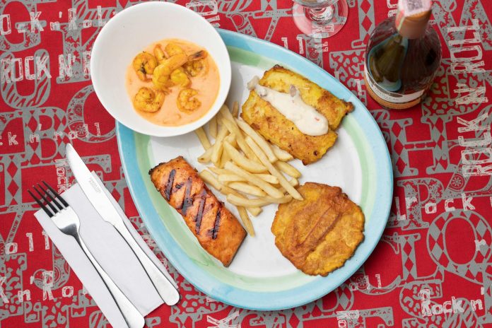 Delicious Colombian seafood platter featuring shrimp, fried plantains, and fish with a creamy sauce.