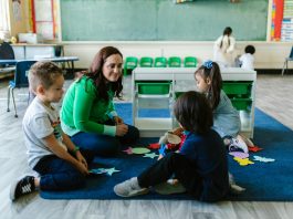 Teacher and children engaged in educational activities on a classroom floor.