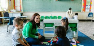 Teacher and children engaged in educational activities on a classroom floor.