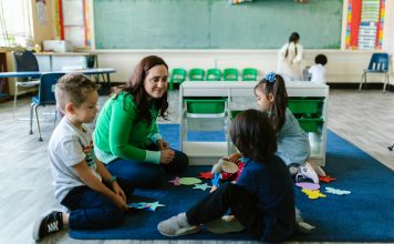 Teacher and children engaged in educational activities on a classroom floor.