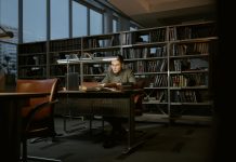A man intensely studies in a quiet library, surrounded by books and soft lighting.