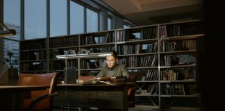A man intensely studies in a quiet library, surrounded by books and soft lighting.
