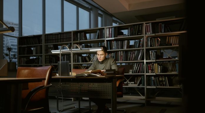 A man intensely studies in a quiet library, surrounded by books and soft lighting.