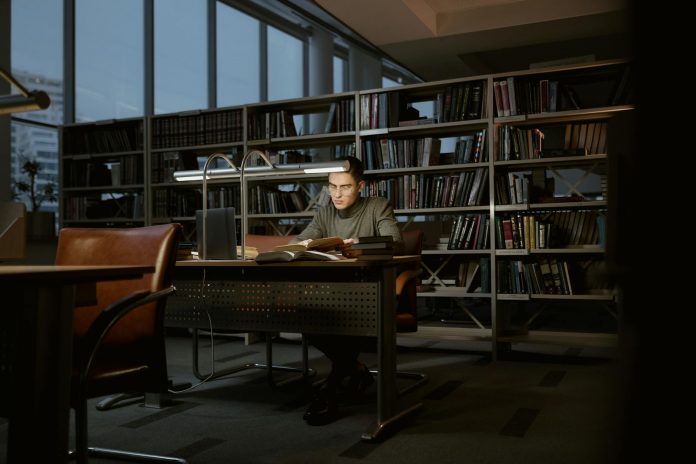 njcu-faculty-union-gives-200k-more-to-support-rese A man intensely studies in a quiet library, surrounded by books and soft lighting.