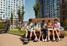 Children sitting on a bench, eating and sharing leisure time outdoors in a modern playground.