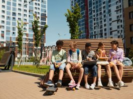 Children sitting on a bench, eating and sharing leisure time outdoors in a modern playground.