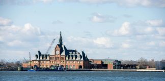 Scenic view of the historic Ellis Island train station with clock tower set against a bright sky.