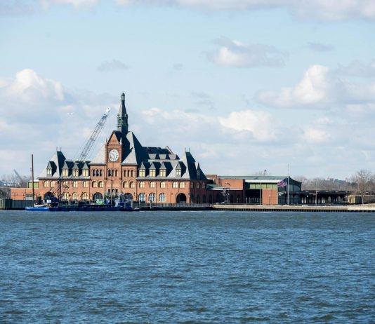 Scenic view of the historic Ellis Island train station with clock tower set against a bright sky.
