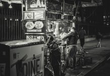 Black and white photo of a food vendor in New York City, capturing urban night life.