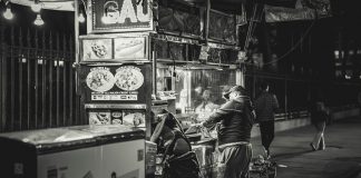 Black and white photo of a food vendor in New York City, capturing urban night life.
