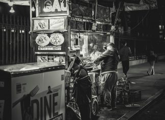 Black and white photo of a food vendor in New York City, capturing urban night life.
