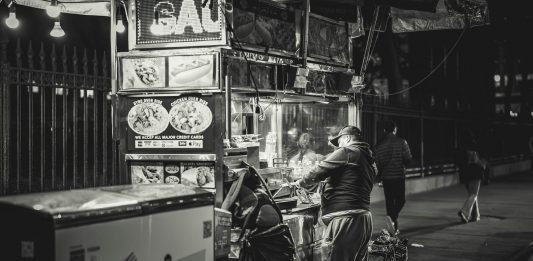 Black and white photo of a food vendor in New York City, capturing urban night life.