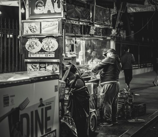 Black and white photo of a food vendor in New York City, capturing urban night life.