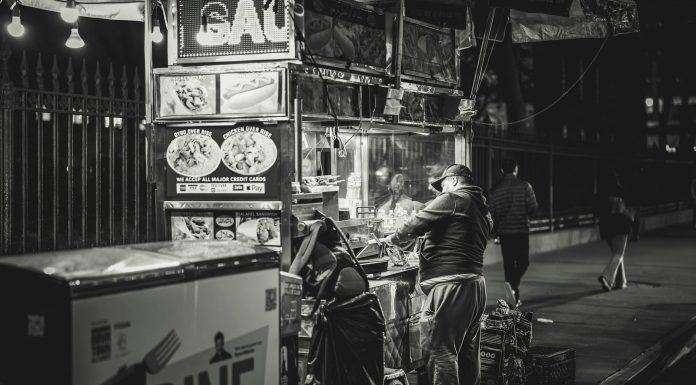 Black and white photo of a food vendor in New York City, capturing urban night life.