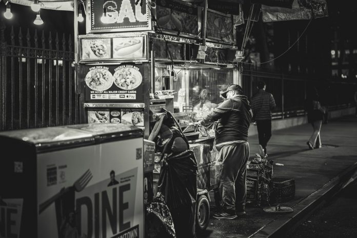 Black and white photo of a food vendor in New York City, capturing urban night life.