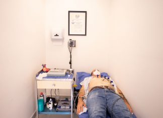Patient lying down for an electrocardiogram in a clinic room wearing a face mask.