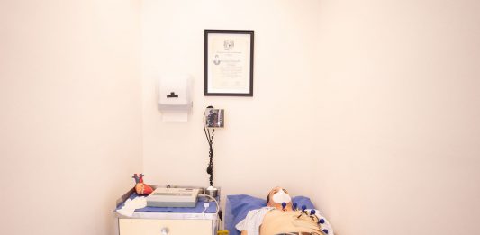 Patient lying down for an electrocardiogram in a clinic room wearing a face mask.