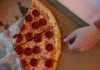 Hand reaching for a delicious pepperoni pizza slice in a cardboard box.