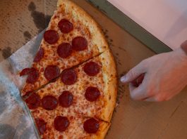 Hand reaching for a delicious pepperoni pizza slice in a cardboard box.