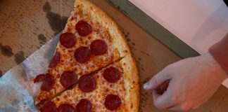 Hand reaching for a delicious pepperoni pizza slice in a cardboard box.