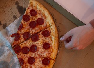 Best Pizza in Elizabeth in 2026: A Local’s Guide to Slices, Pies, and Hidden Gems Hand reaching for a delicious pepperoni pizza slice in a cardboard box.