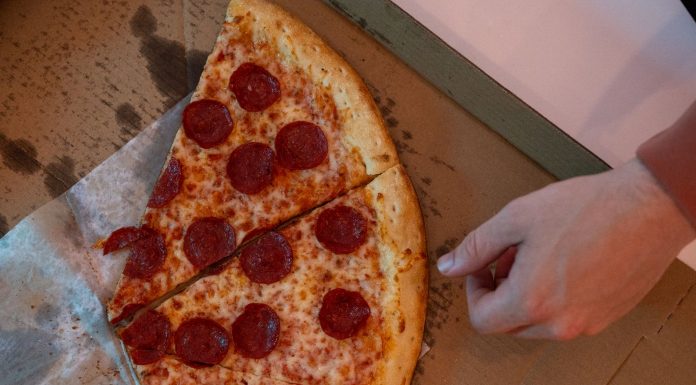 Hand reaching for a delicious pepperoni pizza slice in a cardboard box.