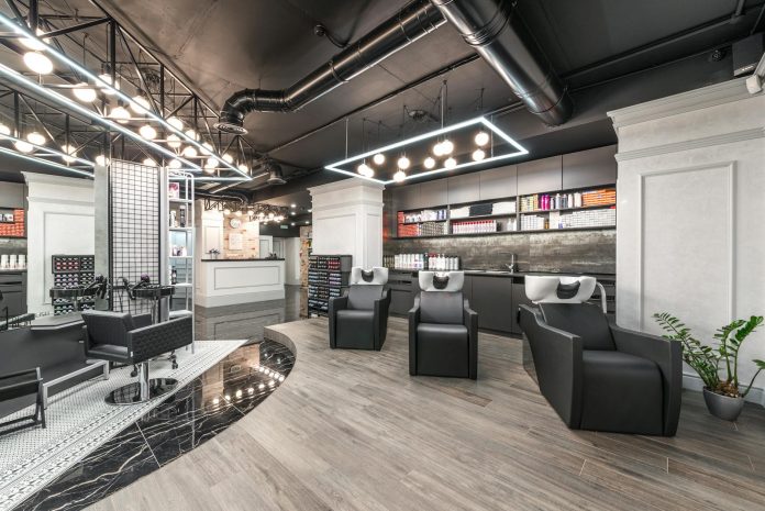Comfortable backwash chairs with sinks near potted plant placed in contemporary beauty salon with bright illumination and abundance of cosmetology products