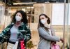 Low angle of woman with purchases in colorful shopping bags walking through doors of store during coronavirus pandemic