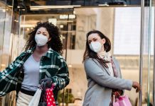Low angle of woman with purchases in colorful shopping bags walking through doors of store during coronavirus pandemic