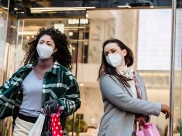 Low angle of woman with purchases in colorful shopping bags walking through doors of store during coronavirus pandemic
