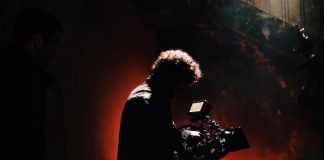 A professional cameraman captures footage in a creatively lit, moody setting, backlit by warm light.