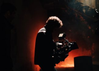 BREAKING: 1888 Studios in Bayonne Wins Major Real Estate Award A professional cameraman captures footage in a creatively lit, moody setting, backlit by warm light.