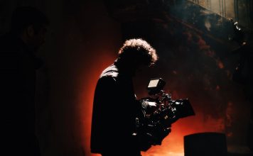 BREAKING: 1888 Studios in Bayonne Wins Major Real Estate Award A professional cameraman captures footage in a creatively lit, moody setting, backlit by warm light.