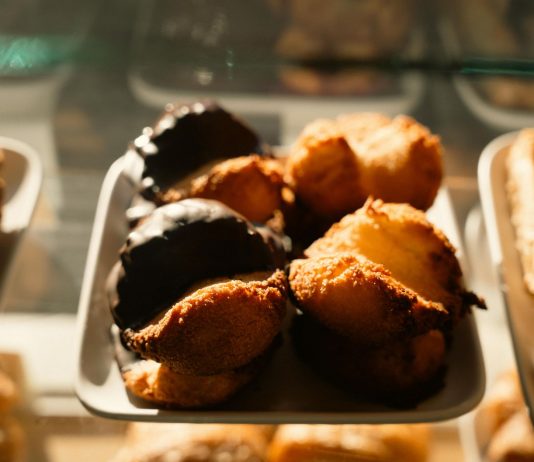 Warm-toned close-up of assorted pastries in a bakery display, sunlight highlighting texture.