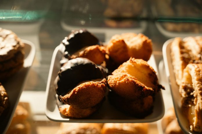 Warm-toned close-up of assorted pastries in a bakery display, sunlight highlighting texture.