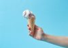 Hand holding a creamy ice cream cone against a vibrant blue background, perfect for summer themes.