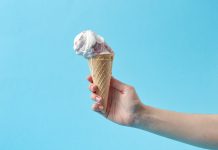 Hand holding a creamy ice cream cone against a vibrant blue background, perfect for summer themes.