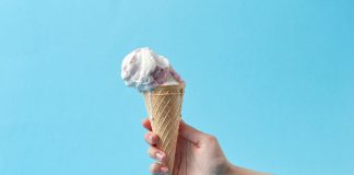Hand holding a creamy ice cream cone against a vibrant blue background, perfect for summer themes.