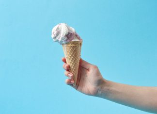 Hand holding a creamy ice cream cone against a vibrant blue background, perfect for summer themes.