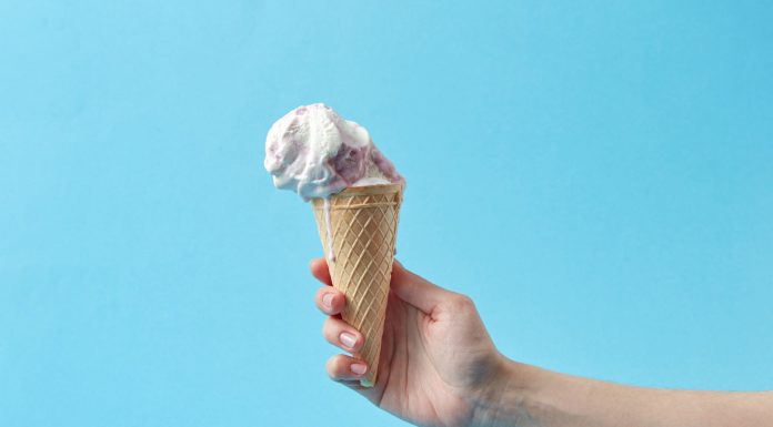 Hand holding a creamy ice cream cone against a vibrant blue background, perfect for summer themes.