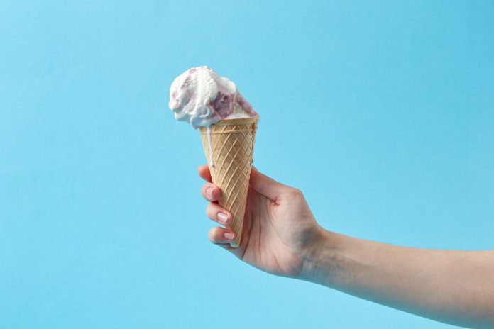 Hand holding a creamy ice cream cone against a vibrant blue background, perfect for summer themes.