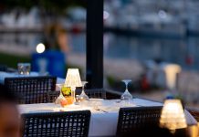 Charming outdoor restaurant setup with lamps and wine glasses by a marina at twilight.