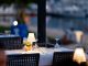 Charming outdoor restaurant setup with lamps and wine glasses by a marina at twilight.