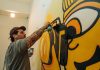 Tattooed artist using spray paint to craft a vibrant indoor graffiti mural.