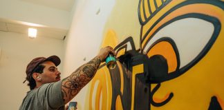Tattooed artist using spray paint to craft a vibrant indoor graffiti mural.