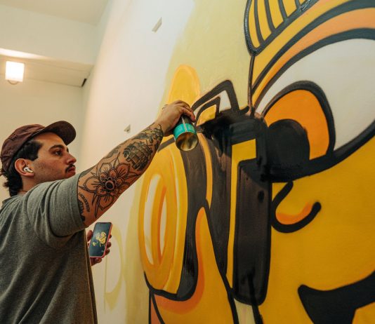 Tattooed artist using spray paint to craft a vibrant indoor graffiti mural.