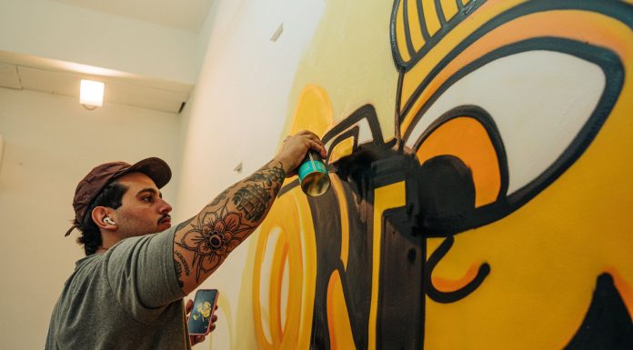 Tattooed artist using spray paint to craft a vibrant indoor graffiti mural.