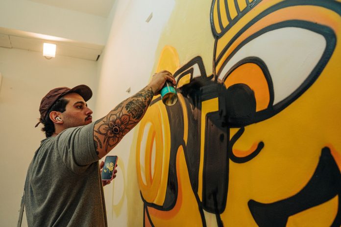 Tattooed artist using spray paint to craft a vibrant indoor graffiti mural.