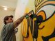 Tattooed artist using spray paint to craft a vibrant indoor graffiti mural.